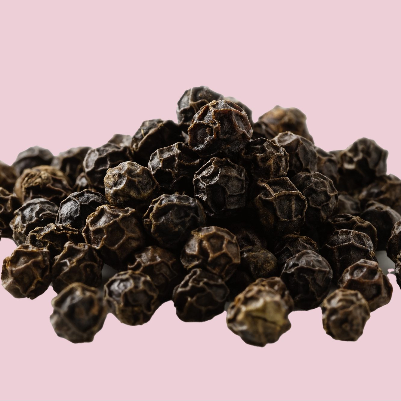 A pile of whole black pepper isolated on white.